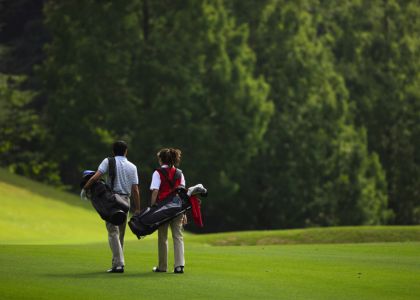 Two golfers walking on a sunny golf course with bags over their shoulders (back view).